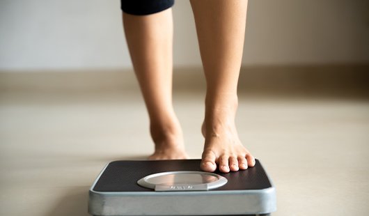 A woman's lower legs stepping onto weighing scales.